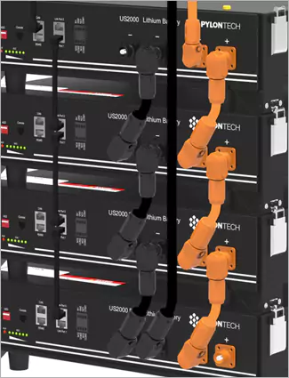 "Close-up of wall-mounted black energy storage batteries or inverters with connected orange and black cabling."